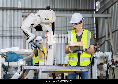 Un team di ingegneri maschili e femminili si riunisce per ispezionare i robot di saldatura dell'acciaio controllati dal computer. Pianificare le prove e l'installazione per l'uso. Foto Stock