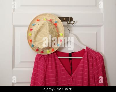 Appendiabiti con blusa e cappello in paglia sulla porta bianca Foto Stock