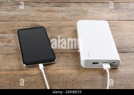 Ricarica del telefono cellulare con power bank su sfondo di legno Foto Stock