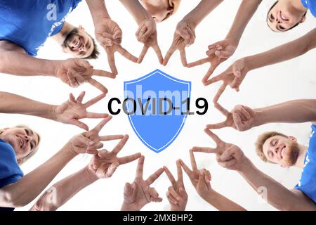 Volontari che si uniscono per aiutare durante l'epidemia di COVID-19. Gruppo di persone che tengono le mani unite, illustrazione dello scudo Foto Stock