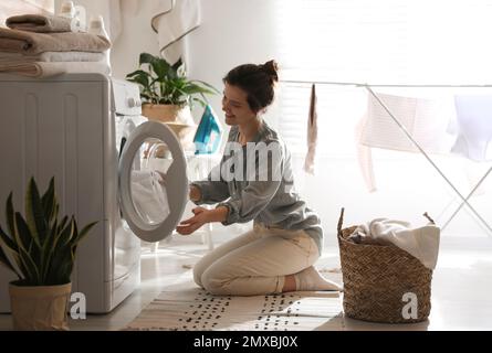 Giovane donna che porta la lavanderia fuori dalla lavatrice a casa Foto Stock