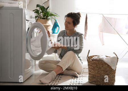 Giovane donna che porta la lavanderia fuori dalla lavatrice a casa Foto Stock