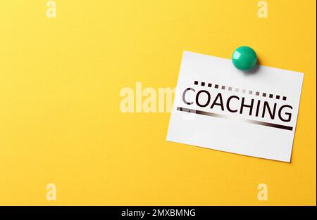 Apprendimento per adulti. Nota cartacea con parola COACHING su sfondo giallo, spazio per il testo Foto Stock