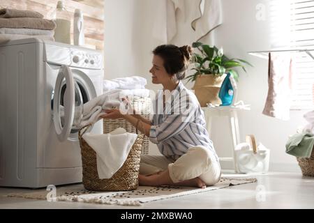 Giovane donna che porta la lavanderia fuori dalla lavatrice a casa Foto Stock