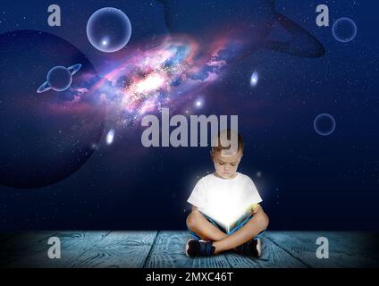 Carino bambino leggere libro magico. Cielo notturno con stelle e pianeti sullo sfondo Foto Stock