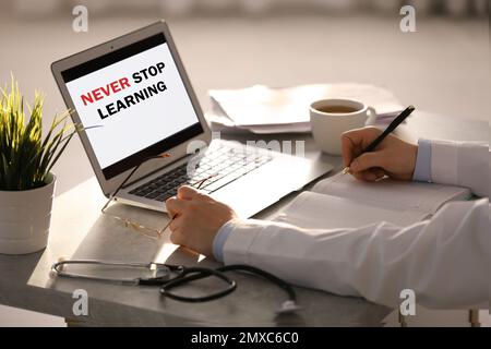 Medico che lavora con il portatile a tavolo in ufficio, primo piano. Non smettere mai di imparare Foto Stock