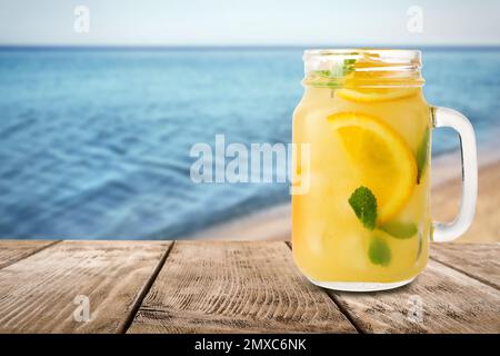 Vaso di Mason con limonata su tavola di legno vicino al mare, spazio per il testo Foto Stock