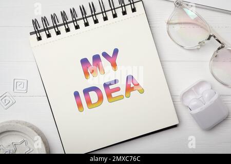 Notebook con parole LA MIA IDEA, occhiali e auricolari su tavolo di legno bianco, piatto Foto Stock