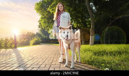 Giovane donna che cammina il suo carino cane Akita Inu nel parco il giorno di sole, banner design. Un animale domestico delizioso Foto Stock