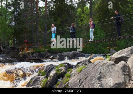 Ruskeala, Russia - 11 giugno 2021: I turisti sono sul ponte sospeso sopra la cascata naturale in una giornata estiva Foto Stock