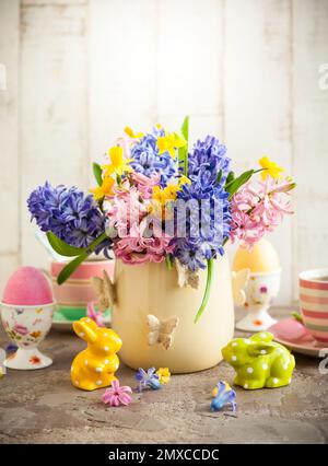 Tavolo per la colazione di Pasqua con tè, uova in coppe d'uovo, fiori primaverili in vaso e decorazioni pasquali Foto Stock