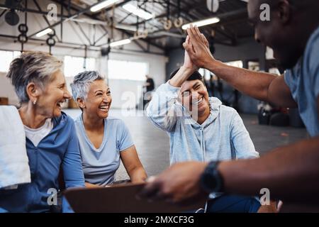 Fitness, donne anziane e personal trainer alto cinque per la salute, la routine e l'allenamento in una palestra. Esercizio fisico, anziani e amici con l'uomo allenatore di salute Foto Stock
