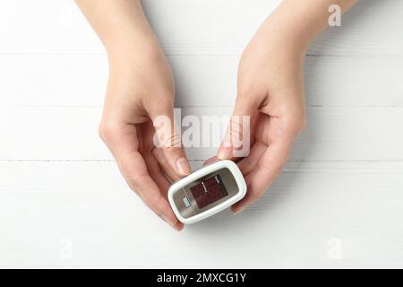 Donna con pulsossimetro FingerTIP su sfondo bianco in legno, vista dall'alto Foto Stock