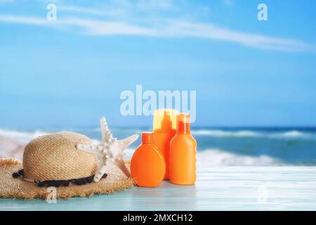 Set di prodotti per la protezione solare e cappello elegante su un tavolo di legno blu vicino al mare. Spazio per il testo Foto Stock