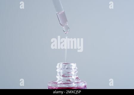 Goccia di olio rosa dal contagocce per pipette in vetro. Macro primo piano per il siero cosmetico di bakuchiol ialuronico con estratto di fico Foto Stock