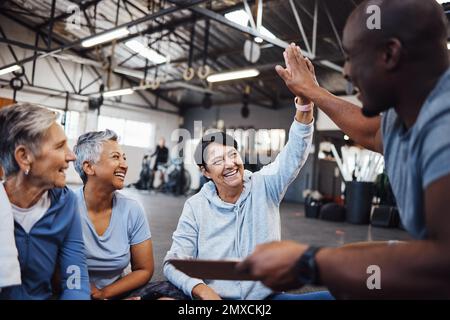 Donne anziane, fitness e personal trainer alto cinque per la salute, la routine e l'allenamento in una palestra. Esercizio fisico, anziani e amici con l'uomo allenatore di salute Foto Stock