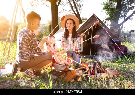 Vacanze scolastiche. Gruppo di bambini felici che friggono salsicce sul falò Foto Stock