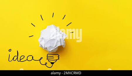 Concetto di idea. Composizione con pallina di carta stropicciata e disegno della lampadina su sfondo giallo, vista dall'alto Foto Stock