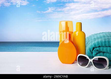 Set di prodotti per la protezione solare ed eleganti occhiali da sole su un tavolo di legno bianco vicino al mare. Spazio per il testo Foto Stock