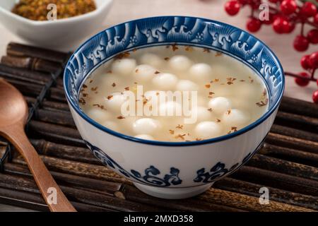 Piccolo tangyuan bianco (tang yuan, palle di gnocchi di riso glutinoso) con miele di osmanthus dolce e zuppa di sciroppo in una ciotola su fondo di tavolo di legno. Foto Stock