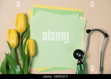 Primavera e medicina - tulipani gialli e stetoscopio con spazio per il testo su sfondo verde chiaro. Foto Stock