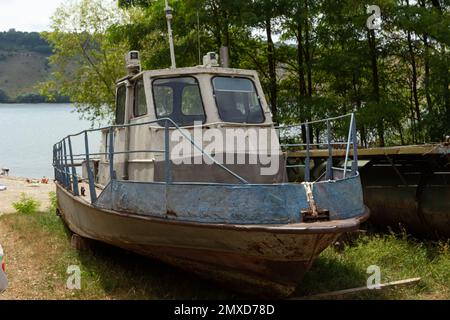 Vecchia barca abbandonata, nave sulla riva sullo sfondo di alberi e fiume. Foto Stock