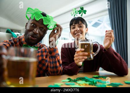 Ritratto di felici amici multirazziali con tazze di birra seduti a tavola, godendo la giornata di san patrizio Foto Stock