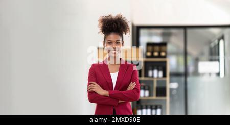 Felice successo femminile professionale sorridente alla fotocamera. La giovane donna d'affari afroamericana con le armi ha attraversato il concetto fiducioso della donna d'affari Foto Stock