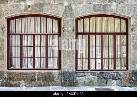 Vecchie finestre ad arco con tende bianche su pareti in pietra dell'edificio storico. Il castello medievale con le mura restaurate attira l'attenzione dei visitatori in arrivo Foto Stock