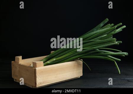 Cipolline fresche verdi in gabbia su tavolo di legno nero Foto Stock