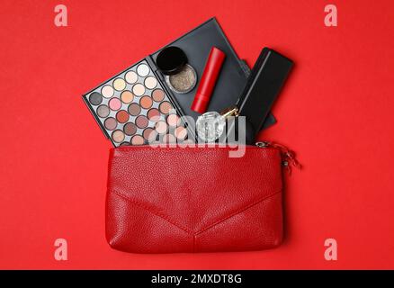 Borsa cosmetica con prodotti per il trucco e profumo su sfondo rosso, piatto Foto Stock