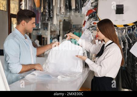 Lavoratore femmina che dà camicia al cliente a secco-pulitore Foto Stock
