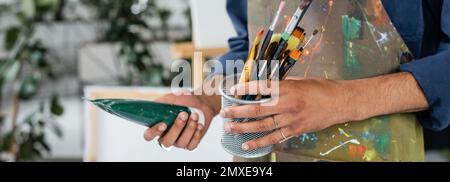 Vista ritagliata dell'artista afrcan americano in grembiule con pennelli e pittura, banner, immagine stock Foto Stock