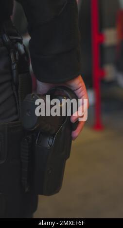 Un colpo verticale di un poliziotto che tiene una pistola nera nella sua custodia Foto Stock