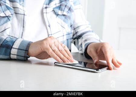Donna che pulisce il telefono cellulare con tampone di cotone al tavolo bianco in interni, primo piano Foto Stock