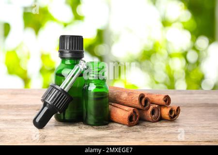 Bottiglie di olio essenziale e cannella bastoni su tavolo di legno su sfondo sfocato Foto Stock