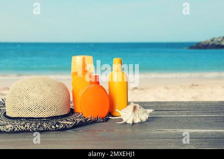 Set di prodotti per la protezione solare e cappello elegante su tavola in legno vicino al mare. Spazio per il testo Foto Stock
