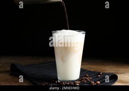 Preparare un delizioso latte macchiato su un tavolo di legno su sfondo nero Foto Stock