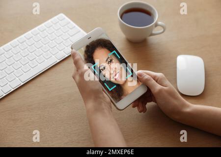 Donna afroamericana che utilizza smartphone con sistema di riconoscimento facciale a tavolo, primo piano. Verifica biometrica Foto Stock