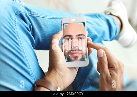Uomo che utilizza lo smartphone con sistema di riconoscimento facciale in interni, primo piano. Verifica biometrica Foto Stock