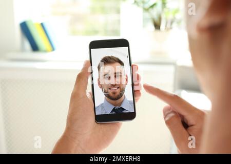 Uomo che utilizza lo smartphone con sistema di riconoscimento facciale in interni, primo piano. Verifica biometrica Foto Stock