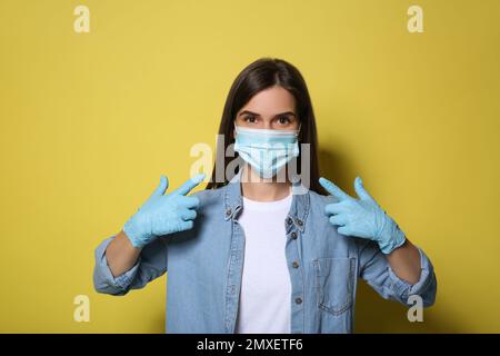 Volontario femminile in maschera e guanti su sfondo giallo. Misure protettive durante la quarantena del coronavirus Foto Stock