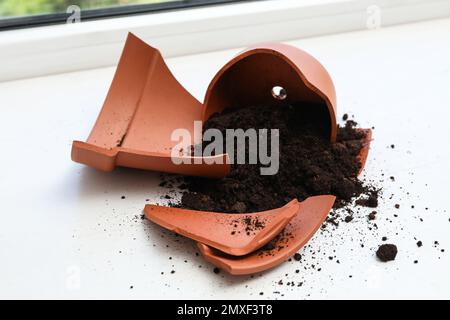Vaso di terracotta rotto con terreno su davanzale bianco al coperto Foto Stock