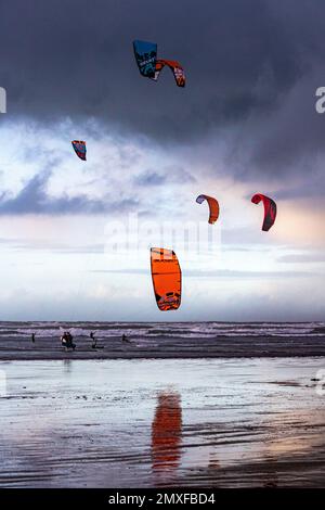 Bright Kites, Wind Surfers, Atlantic Waves, Reflections and a Dark Stormy Sky a Northam Beach, Devon (Vista Ritratto) Foto Stock