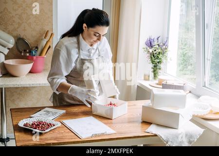 Panetteria piccola impresa locale. Torte speciali per matrimoni, compleanni e anniversari. Il panettiere femminile crea la torta in cucina panetteria. Foto Stock