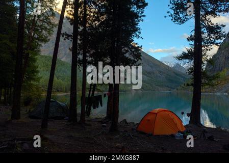 Due tende turistiche si trovano nella foresta sulle rive del lago Shavlinskoye ad alta quota con abiti turistici su una corda. Foto Stock