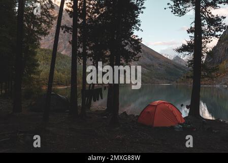 Due tende turistiche si trovano nella foresta, sulla riva del lago di alta quota Shavlinskoe, con abiti turistici che si asciugano su una corda la sera Foto Stock