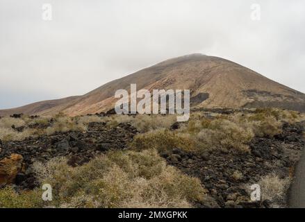 Vecchio cono vulcanico circondato da lava a Lanzarote Foto Stock