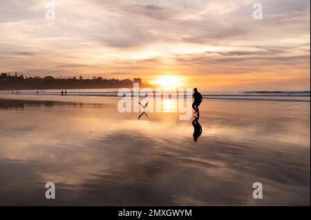 Un uomo cammina verso l'acqua al tramonto su una spiaggia Foto Stock