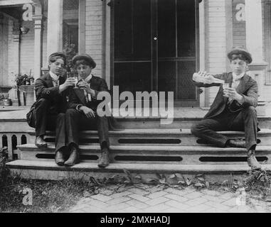 Primi anni '1900 Fotografia d'epoca di giovani uomini su Porch Steps, che condividono bevande in un classico abbigliamento edoardiano - rara immagine originale in bianco e nero di giovani americani che socializzano all'aperto Foto Stock